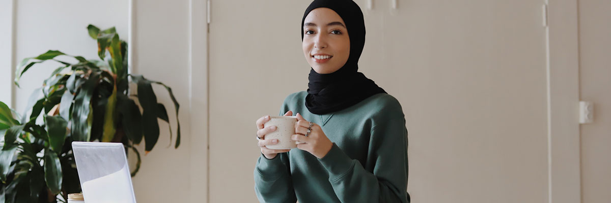 A woman holding a mug in front of her laptop working from home.