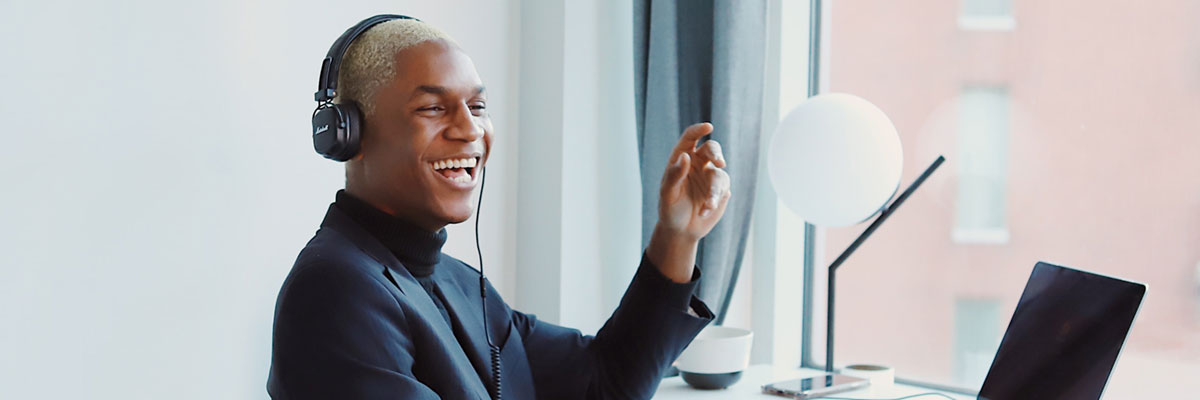 A man with a headset on working at his laptop and laughing.