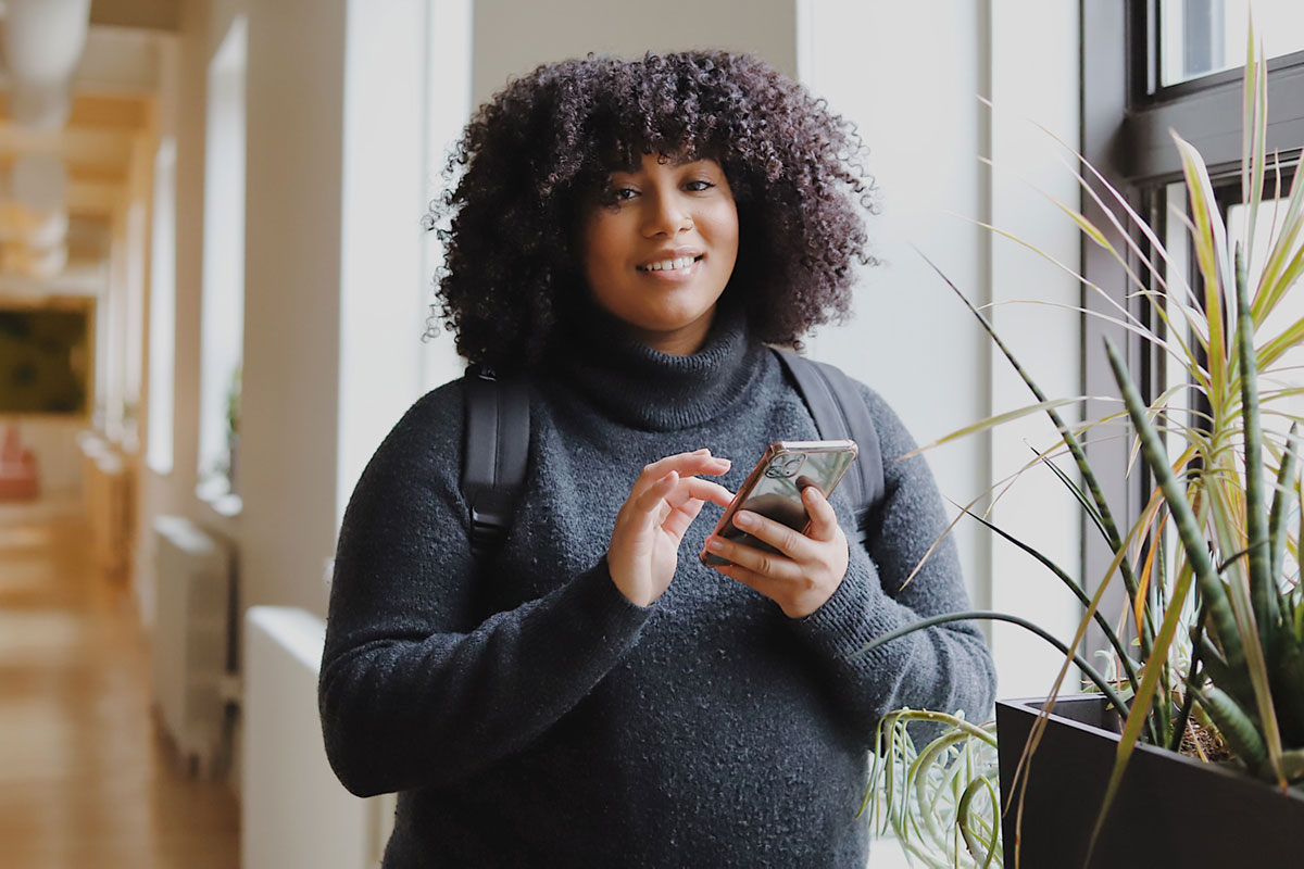 A woman holding her cellphone smiling looking at the camera.